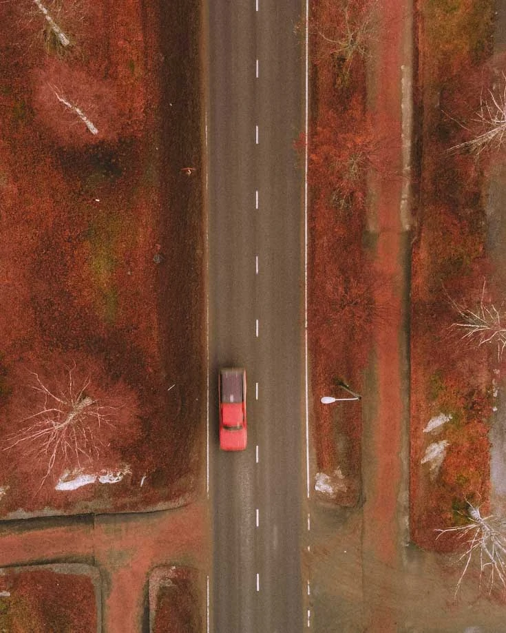 An aerila image of a red campervan driving down a straight road with autumnal colours