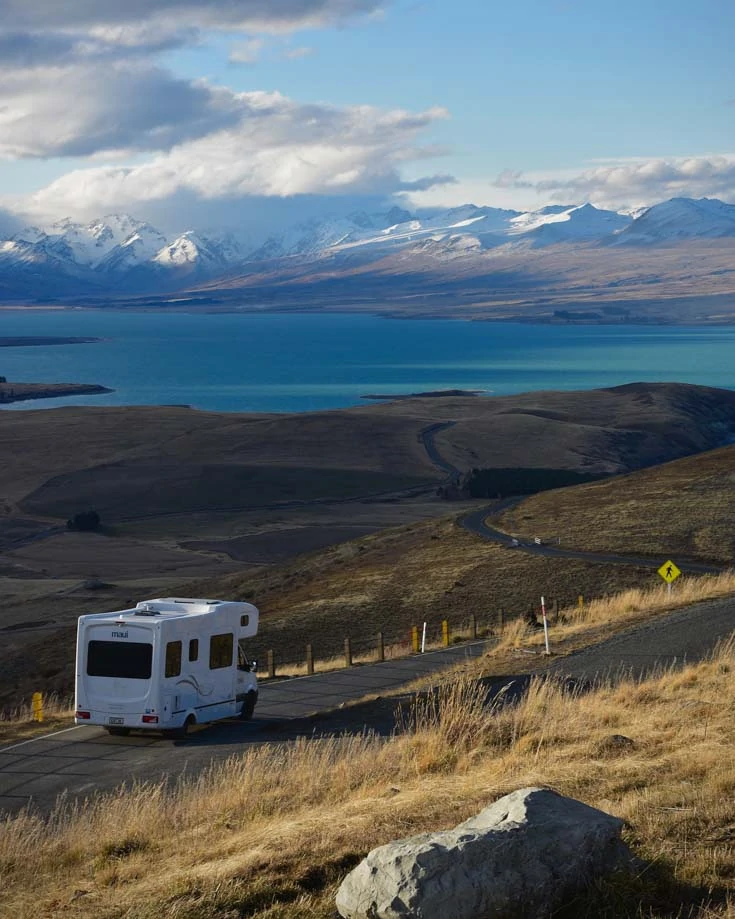 An rv driving through a remote mountain view beside a lake
