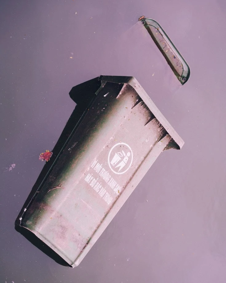 a trash bin discarded in grey dirty water