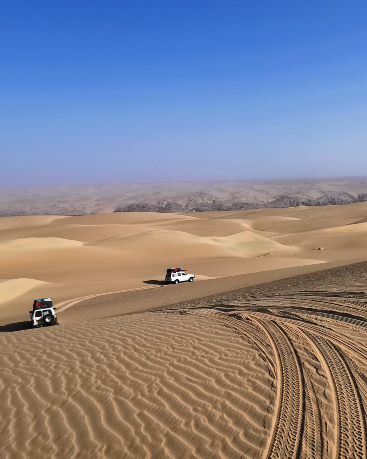 Overland vehicles driving over sand dunes in the desert
