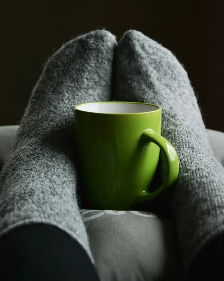 A pair of feet with grey socks hugging a green mug