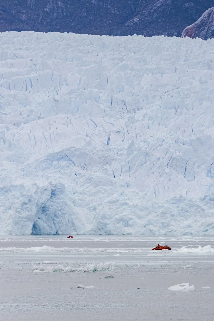 2 zodiacs full of passengers are dwarfed by the massive blue walls of San Rafael glacier in Patagonia's northern Ice Cap