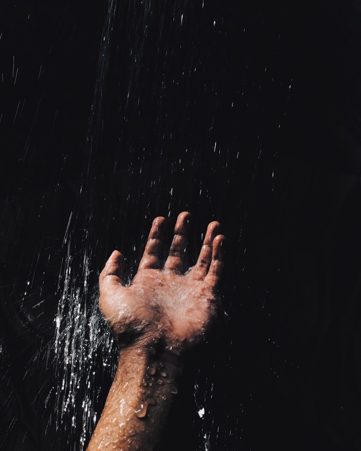 a hand under running cold camp shower water