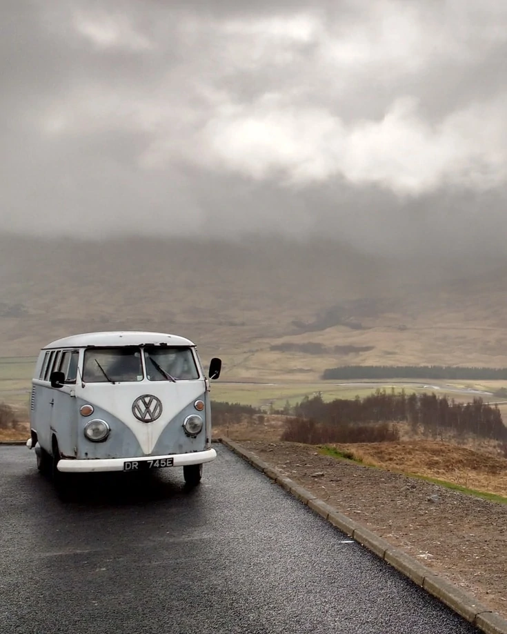 a retro VW camper parked up on a cloudy day overlooking a drab countryside scene