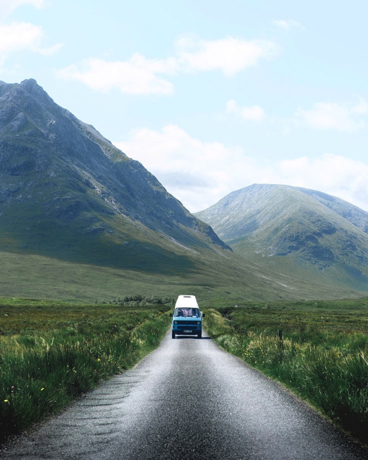 a campervan drivin on a narrow lane surrounded by mountains