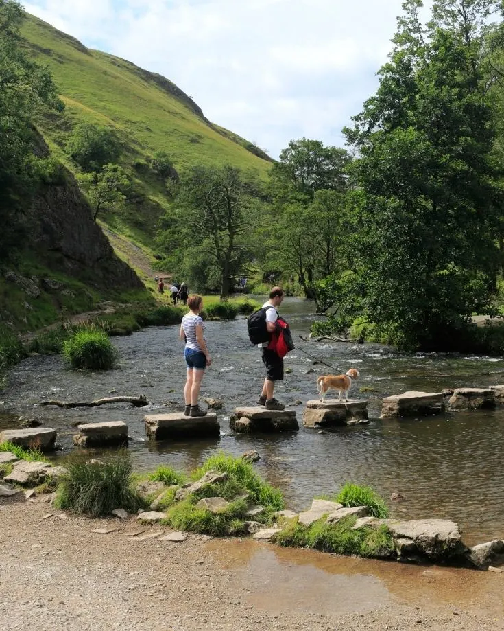 Hikers and their dog crossing the Stepping Stone over the River Dove