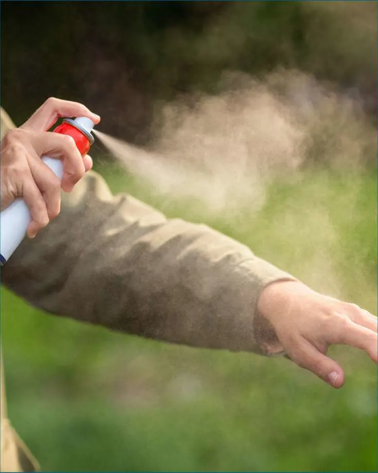 A person spraying permethrin on camping gear to repel mosquitos